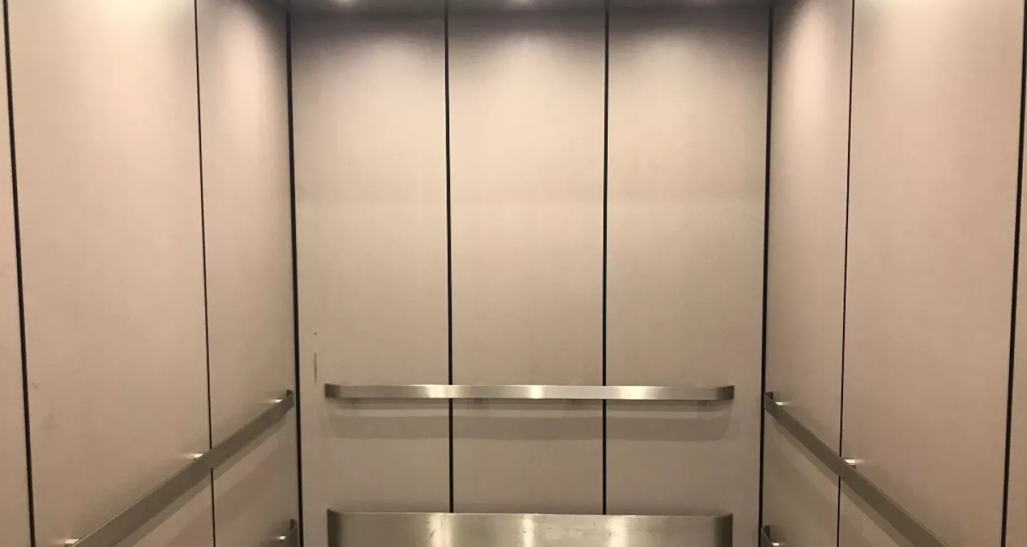 NYC elevator with white walls and stainless steel arm rails